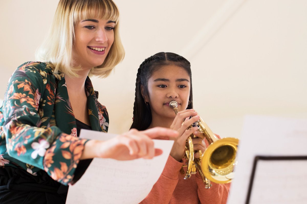 Une enseignante souriante instruisant une jeune fille jouant de la trompette.