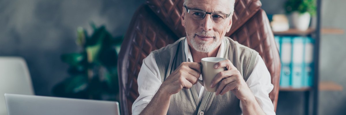Distinguished looking man sitting in a leather chair at his desk holding a coffee mug.