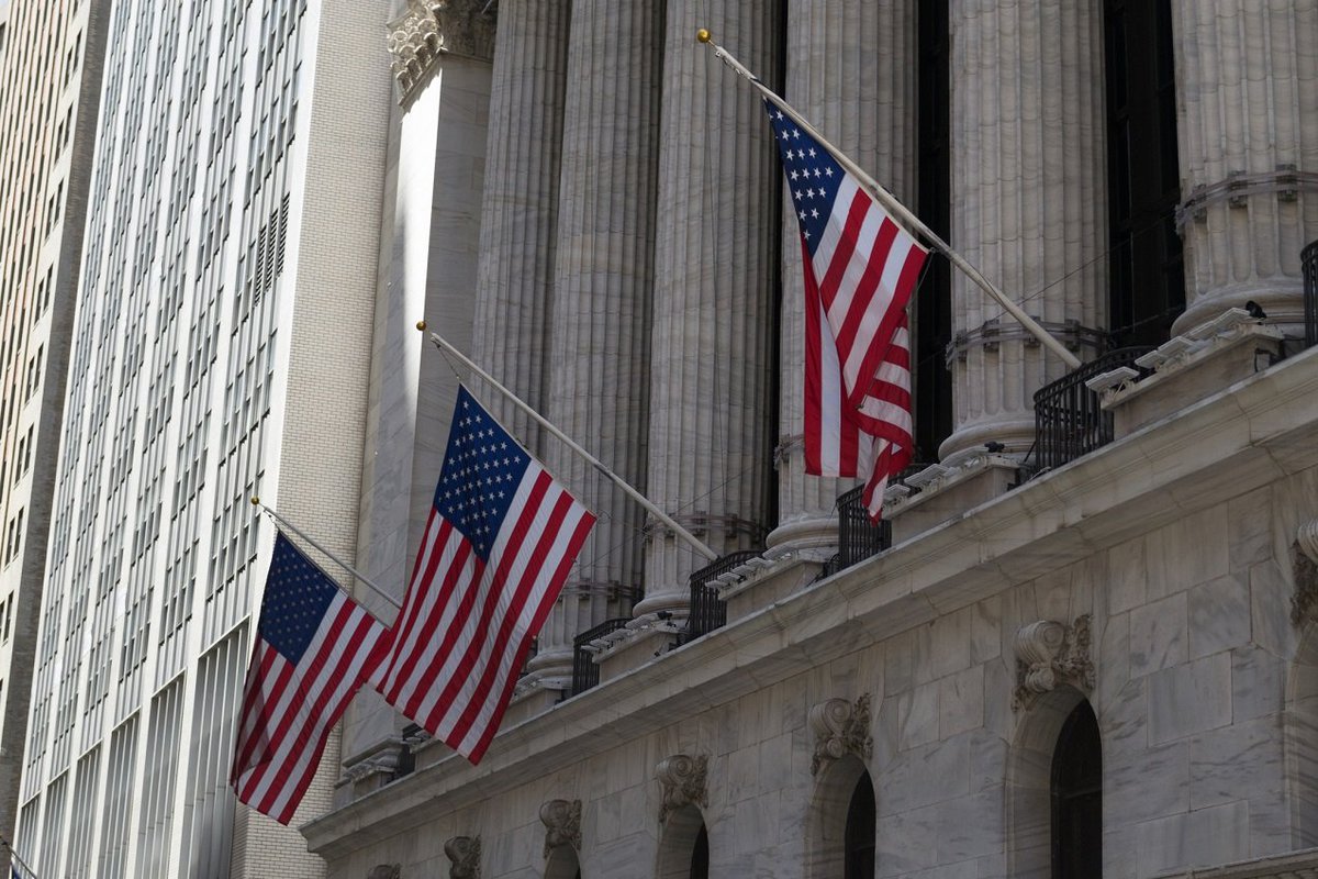 Three American flags hanging from building with concrete pillars.