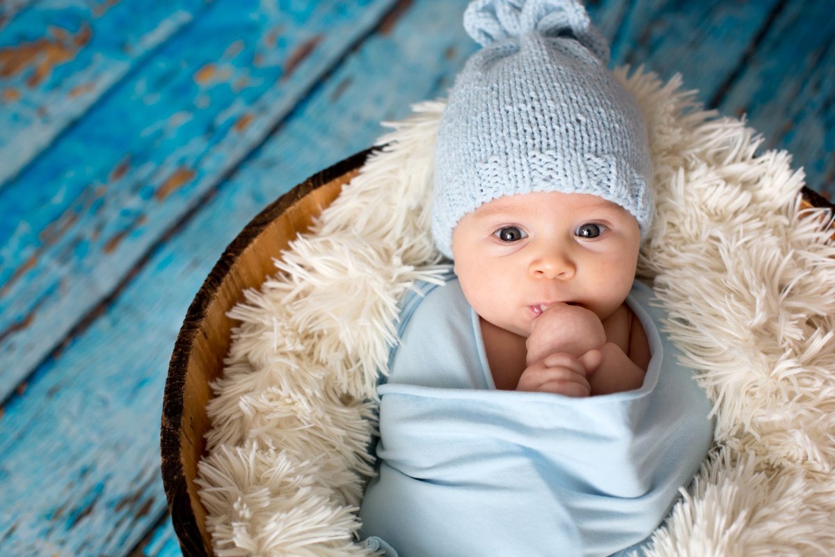 A baby swaddled in a blue blanket and hat.