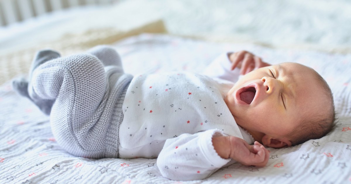 A newborn baby lying in a crib and yawning.