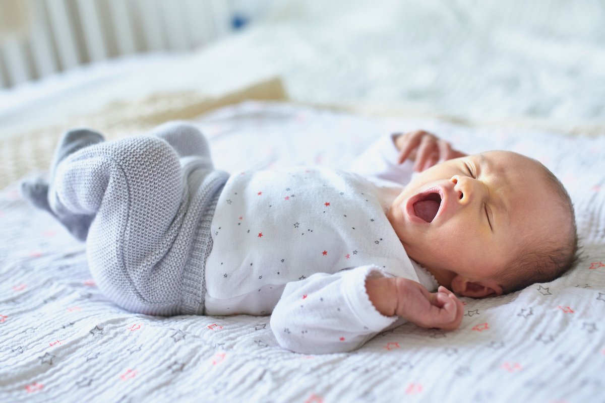A newborn baby lying in a crib and yawning.