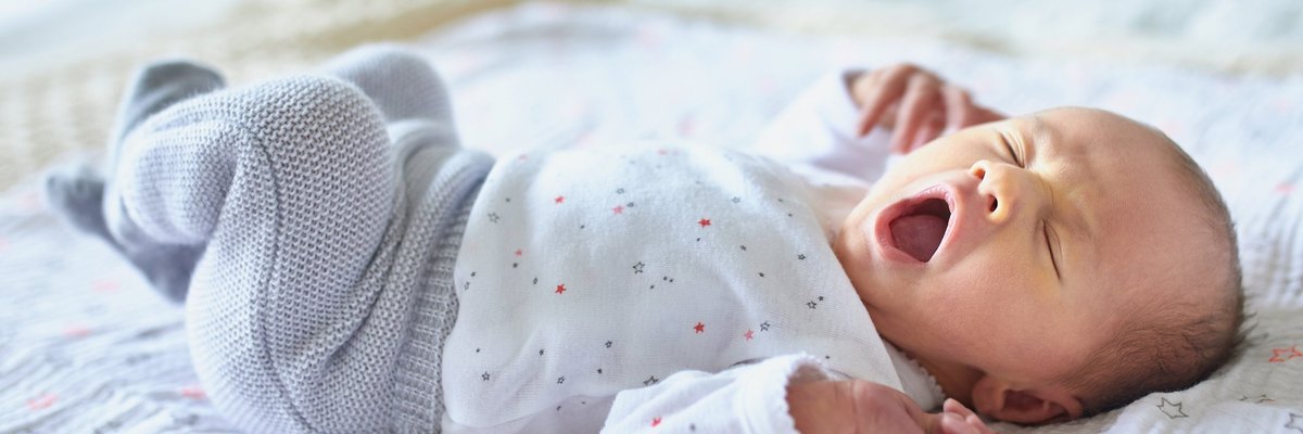 A newborn baby lying in a crib and yawning.