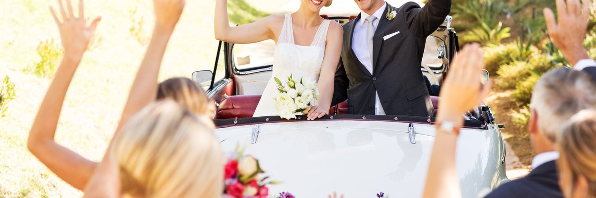 Newlywed couple in the back of a car decorated with a Just Married banner.