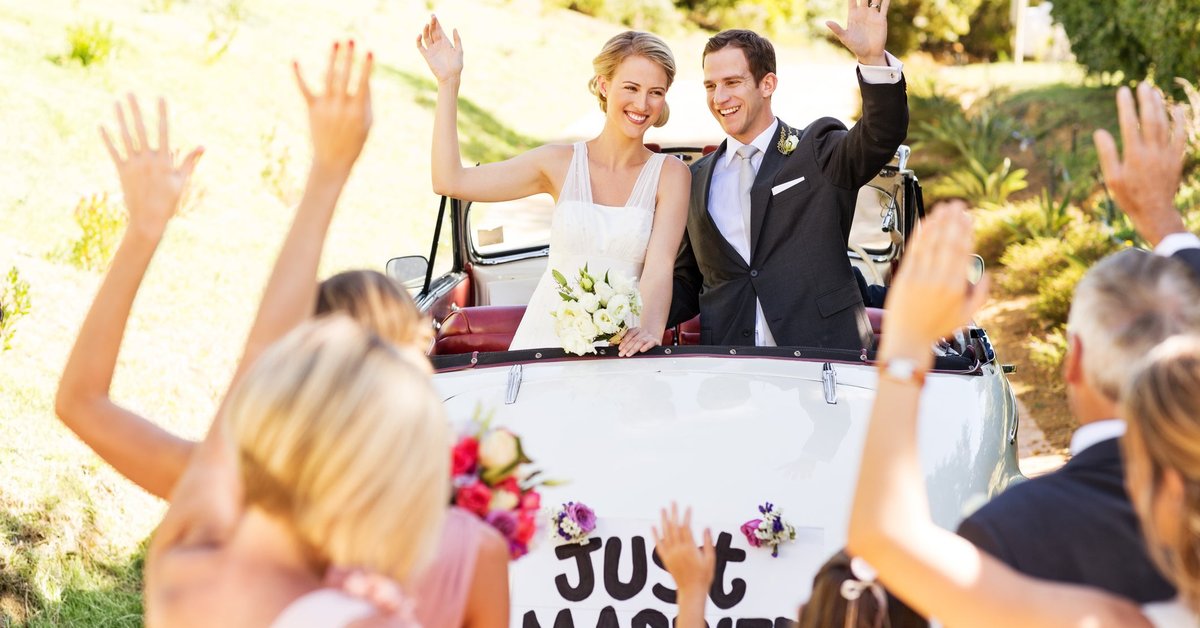 Newlywed couple in the back of a car decorated with a Just Married banner.