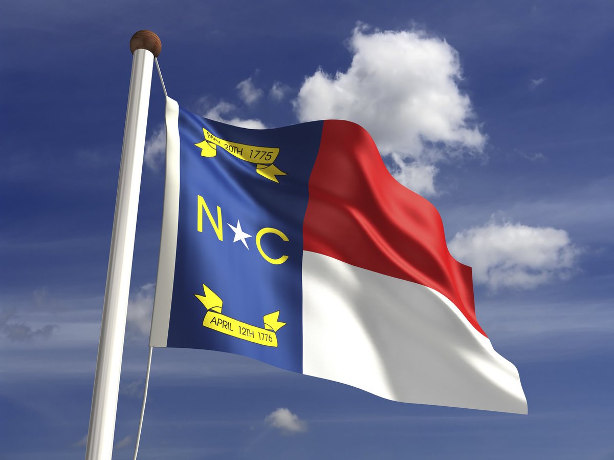 The North Carolina state flag in front of a blue sky with white clouds.