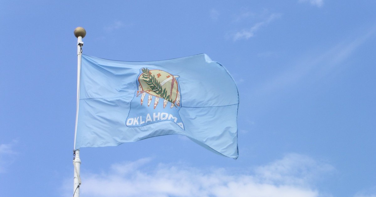 The Oklahoma state flag in front of a blue sky and white clouds.