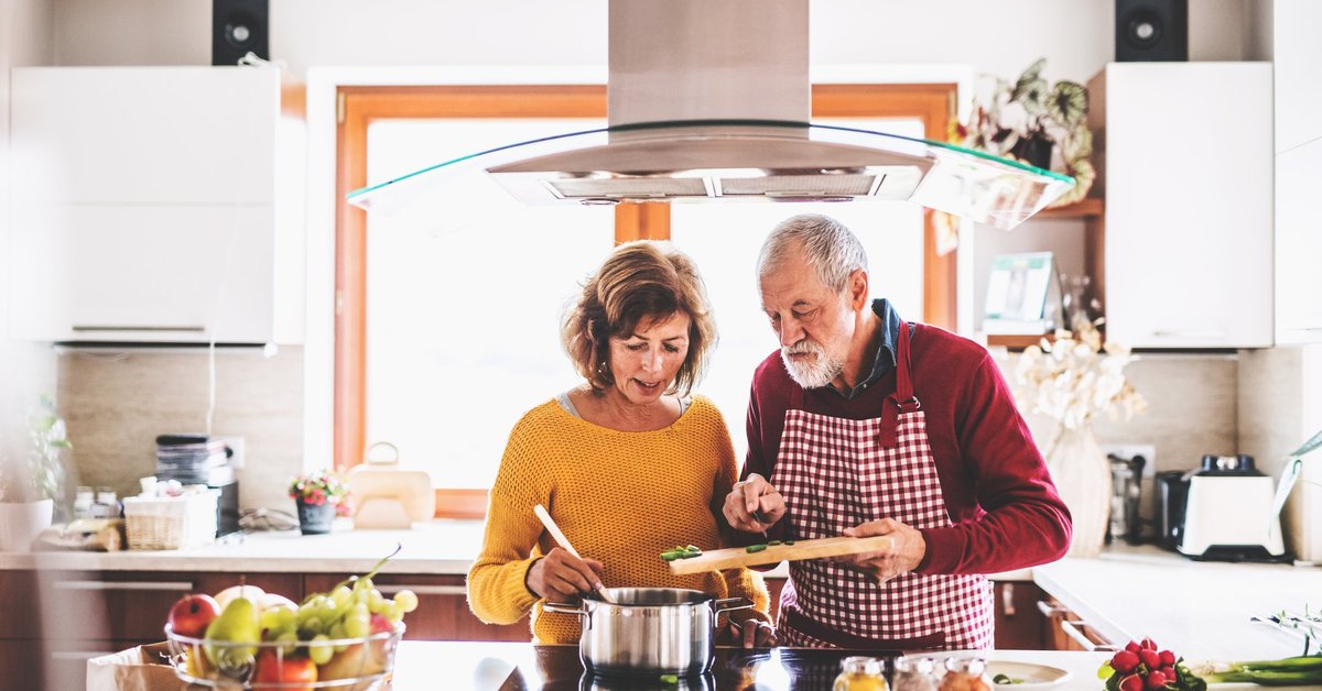 A husband and wife cooking together at the stove.