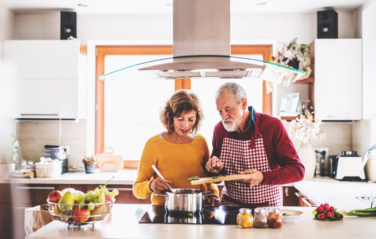 A husband and wife cooking together at the stove.