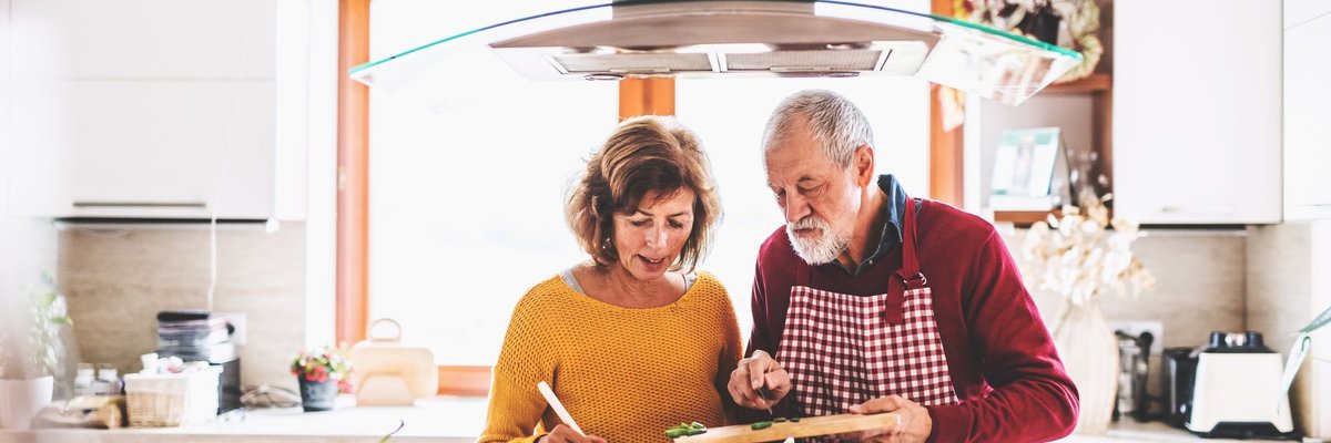 A husband and wife cooking together at the stove.
