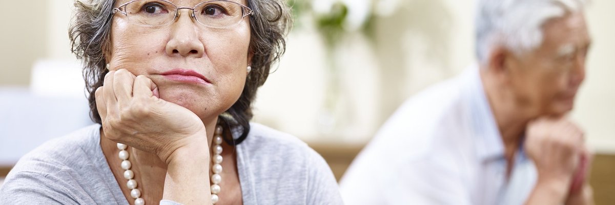 An older couple looking stressed and facing away from each other on a couch.