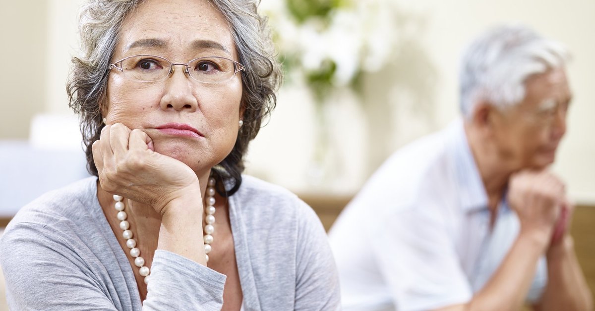 An older couple looking stressed and facing away from each other on a couch.