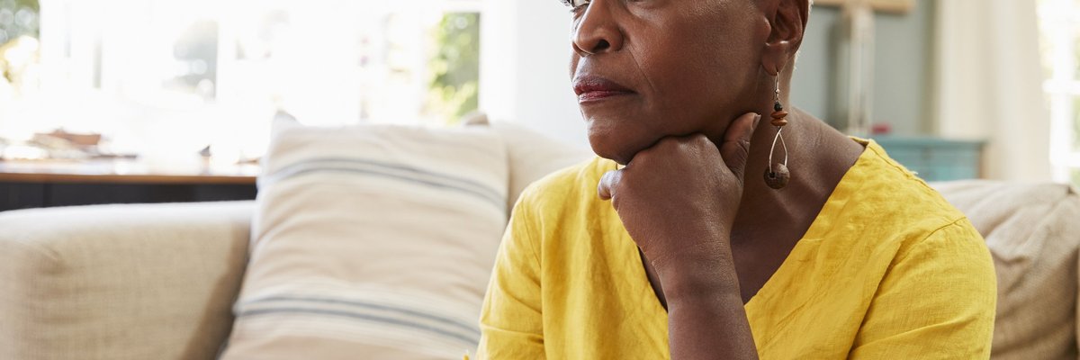 An older woman sitting on the couch and looking stressed.