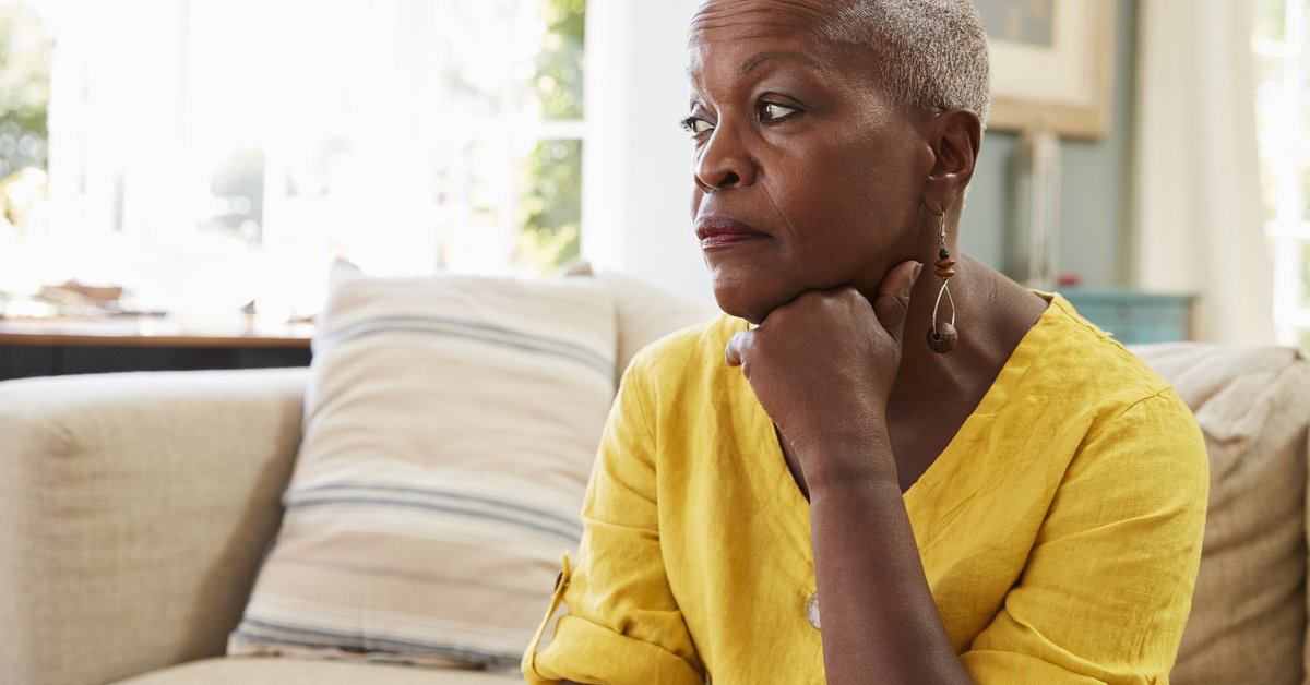 An older woman sitting on the couch and looking stressed.