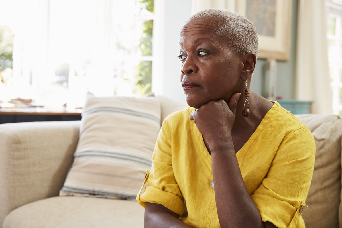 An older woman sitting on the couch and looking stressed.