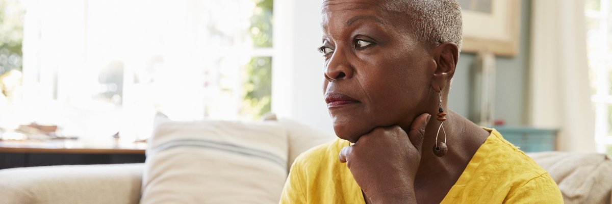 An older woman sitting on the couch and looking stressed.