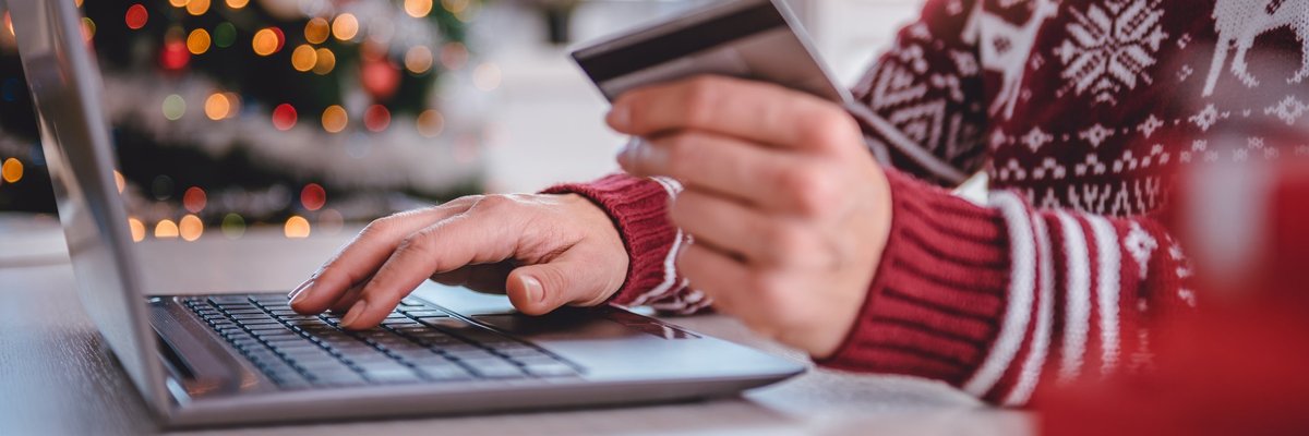 A person in a holiday sweater holding a credit card while typing on a laptop.