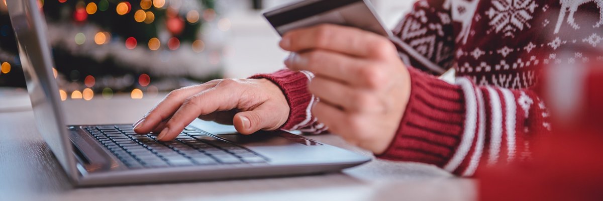 A person in a holiday sweater holding a credit card while typing on a laptop.