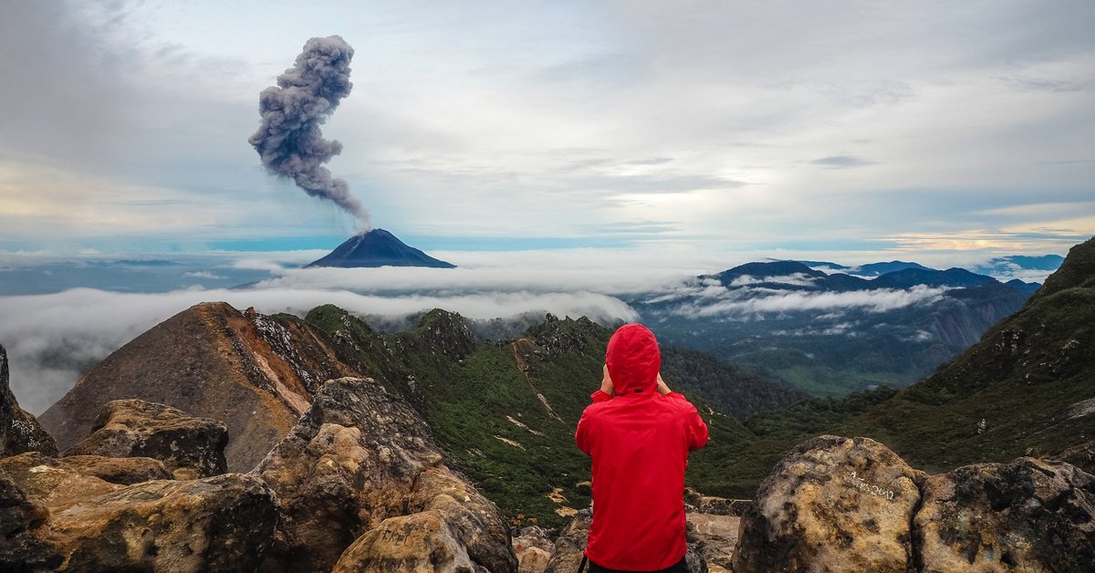 Onlooker photographing an erupting volcano from afar.