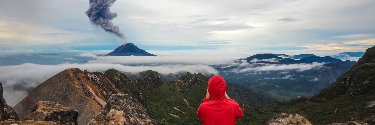 Onlooker photographing an erupting volcano from afar.