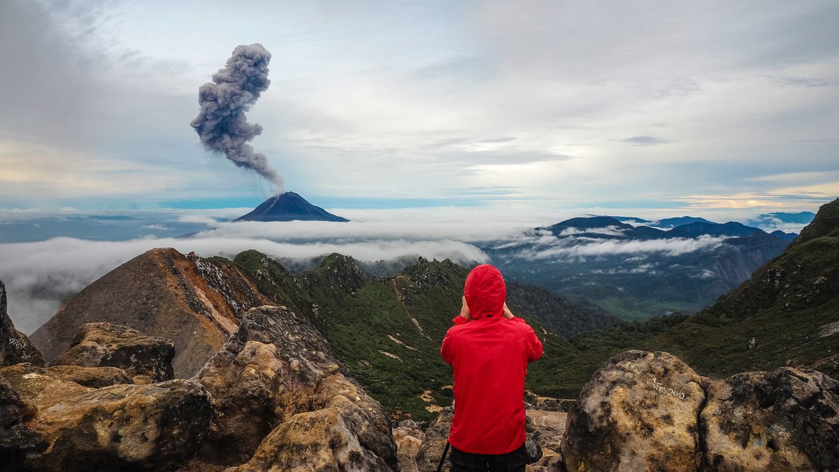 Onlooker photographing an erupting volcano from afar.