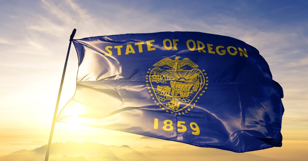 The state flag of Oregon flying in front of a sunny sky.