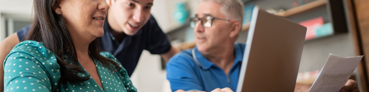 A child offers cryptocurrency advice to his parents who sit at a computer, looking over their personal finances.
