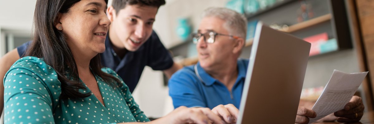 A child offers cryptocurrency advice to his parents who sit at a computer, looking over their personal finances.