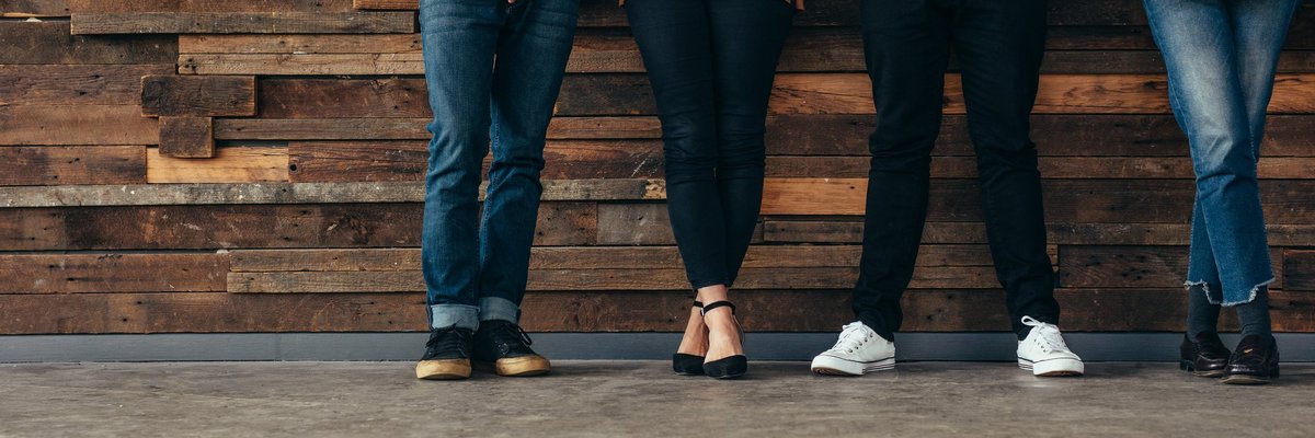 Four people standing against a rustic wood wall.