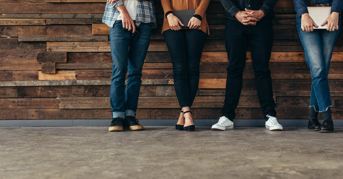 Four people standing against a rustic wood wall.