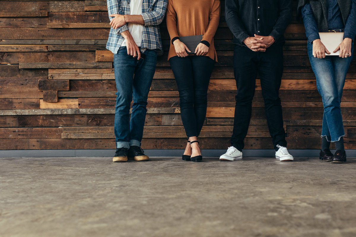 Four people standing against a rustic wood wall.