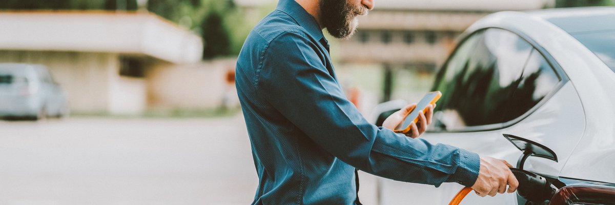 Person connecting their EV to power source while looking at cellphone