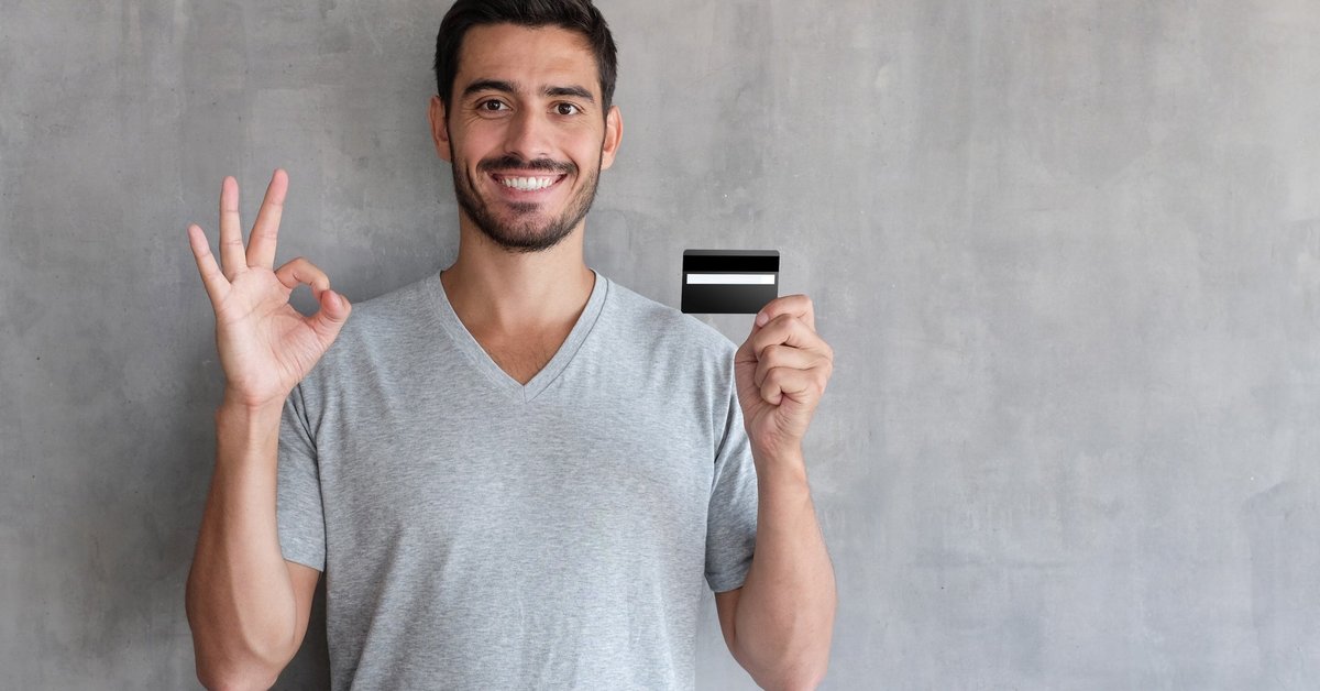 A smiling person holding a credit card.