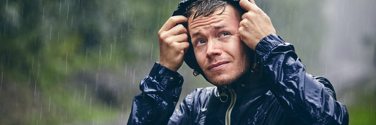 Person outside in a rain storm pulling up the hood on their rain coat.