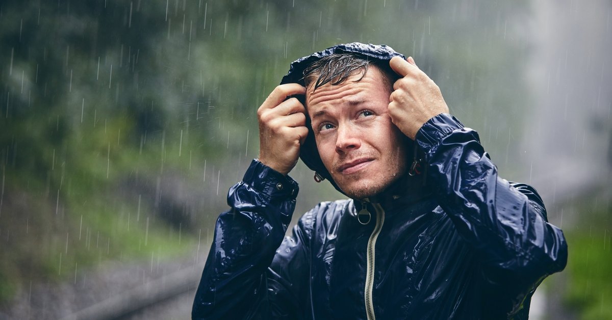 Person outside in a rain storm pulling up the hood on their rain coat.