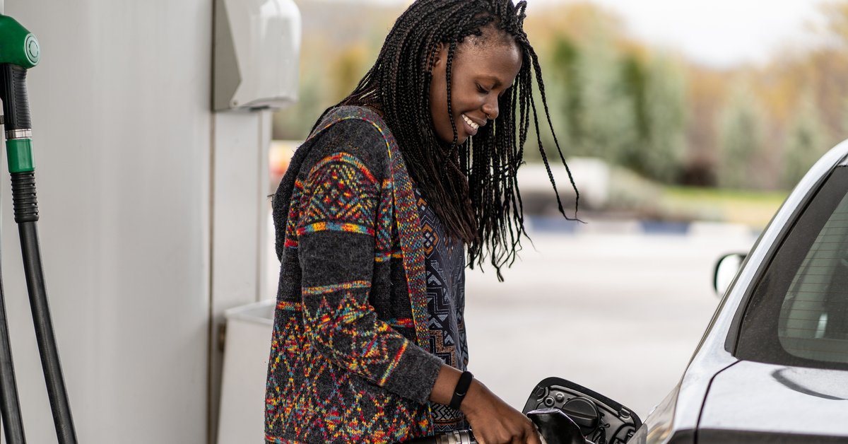 Person smiling while pumping fuel into vehicle's gas tank.