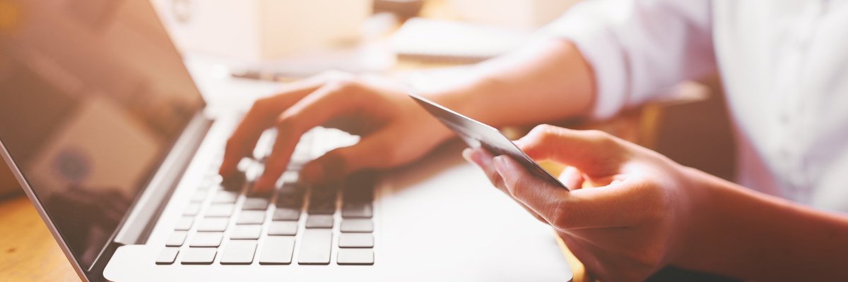 A person using a laptop while holding a credit card.