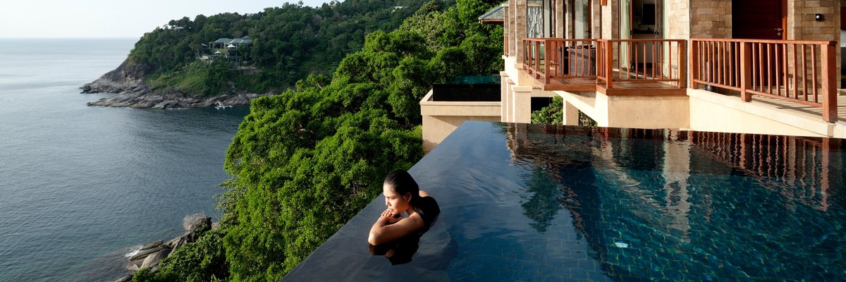 Woman in infinity pool at luxury resort overlooking cliffside and ocean.