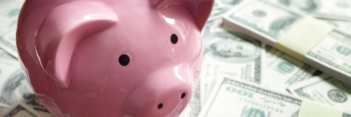 Pink piggy bank on top of piles of hundred dollar bills.