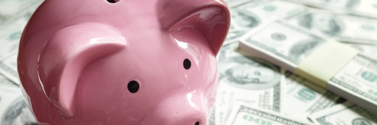 Pink ceramic piggy bank sitting on a pile of paper money