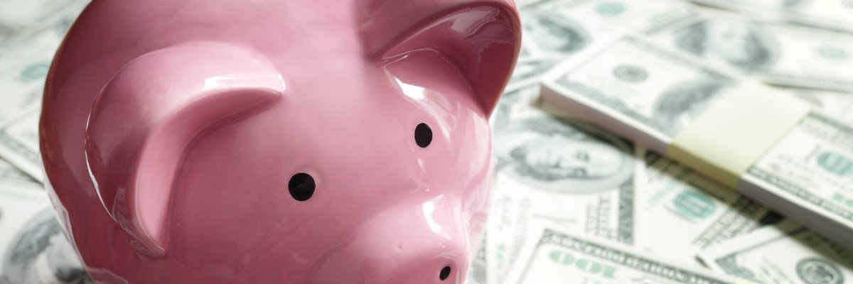 Pink piggy bank on top of piles of hundred dollar bills.