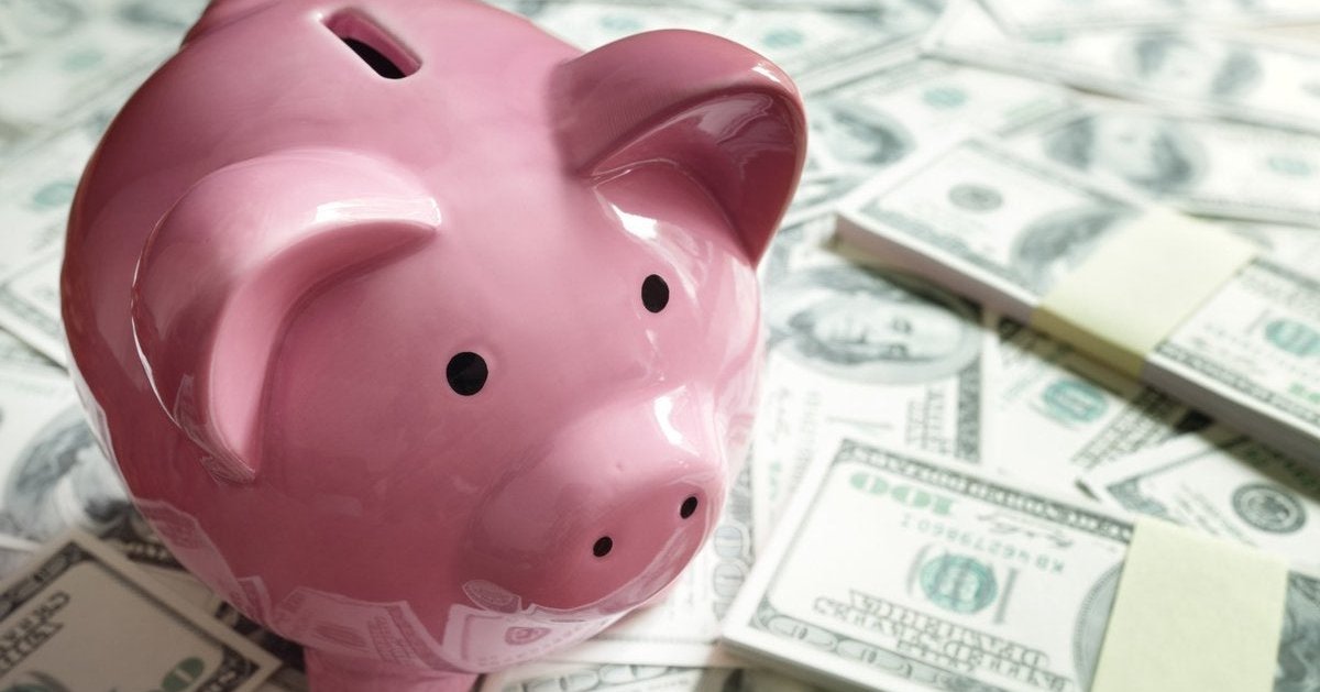 Pink ceramic piggy bank sitting on a pile of paper money