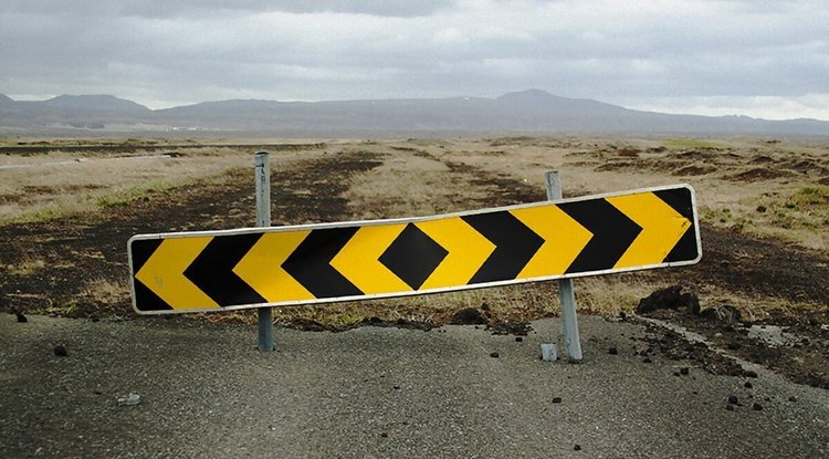 End of the road sign at the end of a street with an open field.