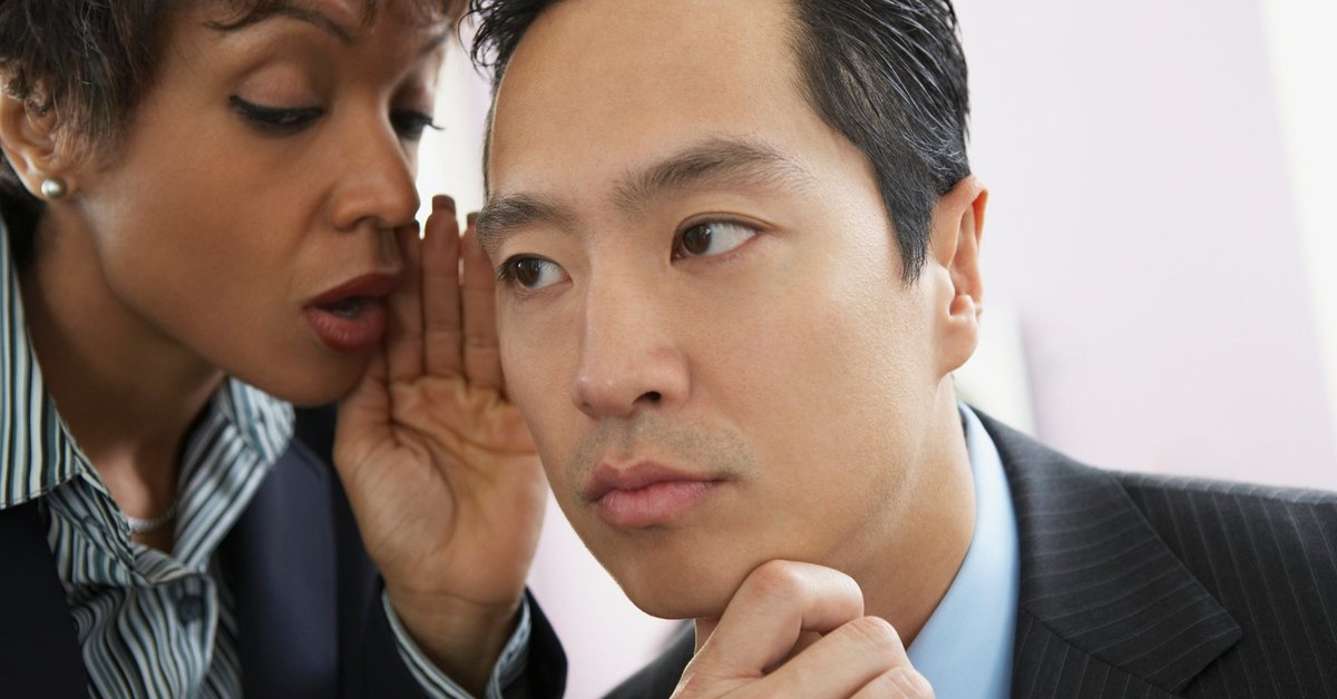 Professionally dressed woman whispering in the ear of professionally dressed man.