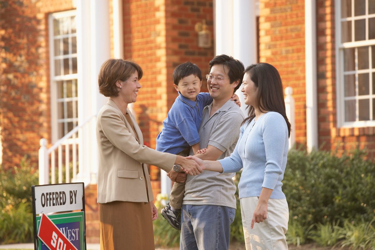 A real estate agent shakes hands with a family with a sold sign outside.