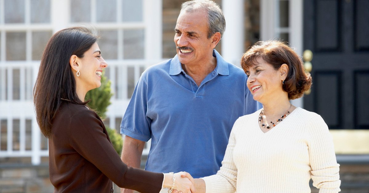 Realtor shaking hands with mature couple outside home.