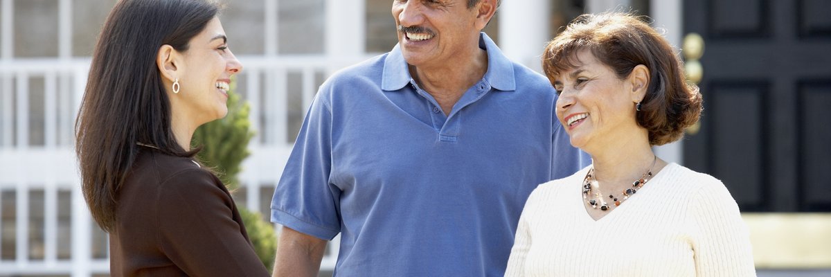 Realtor shaking hands with mature couple outside home.