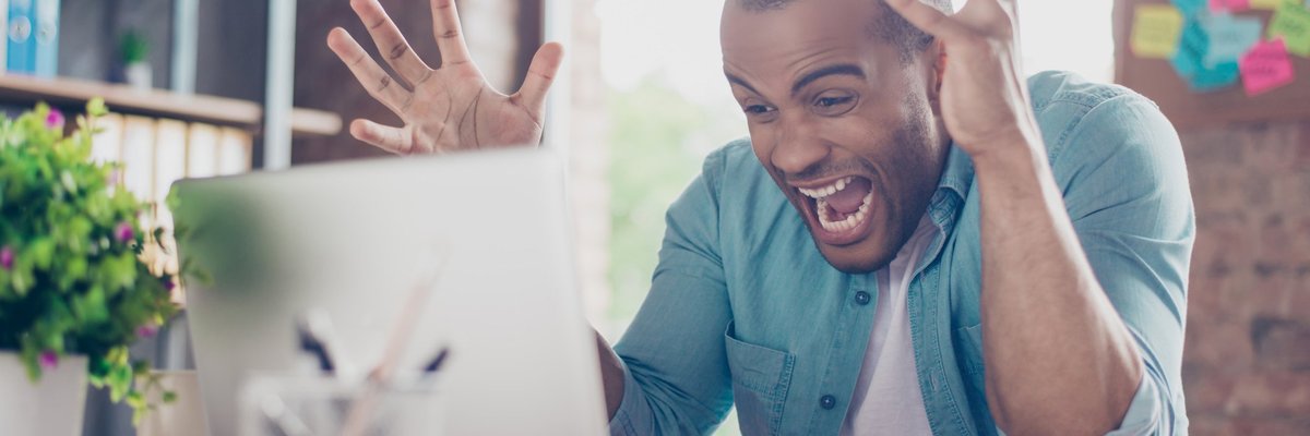 Man in shock yelling at laptop with hands in the air.
