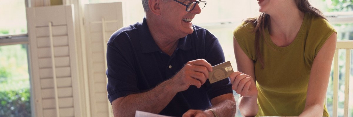 Smiling father handing credit card to teenage daughter.