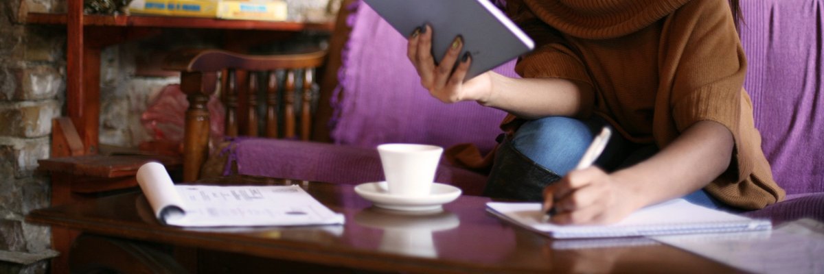 Woman using tablet and writing on a notepad.